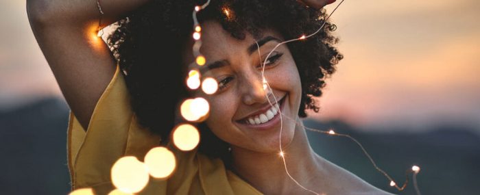 Boost your Confidence: Overcome Fear and Anxiety to Step into Life - Woman smiling confidently while holding a string of lights, RebeccaRoberts.com