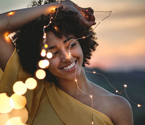 Boost your Confidence: Overcome Fear and Anxiety to Step into Life - Woman smiling confidently while holding a string of lights, RebeccaRoberts.com